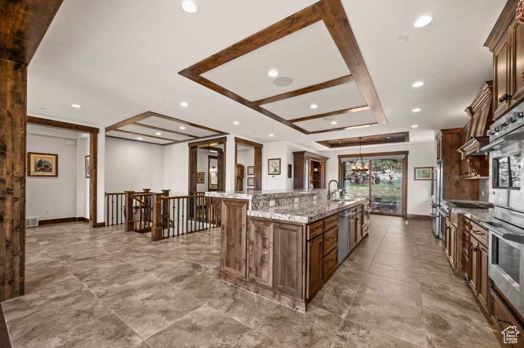 Kitchen featuring light tile floors, sink, light stone countertops, a large island, and hanging light fixtures