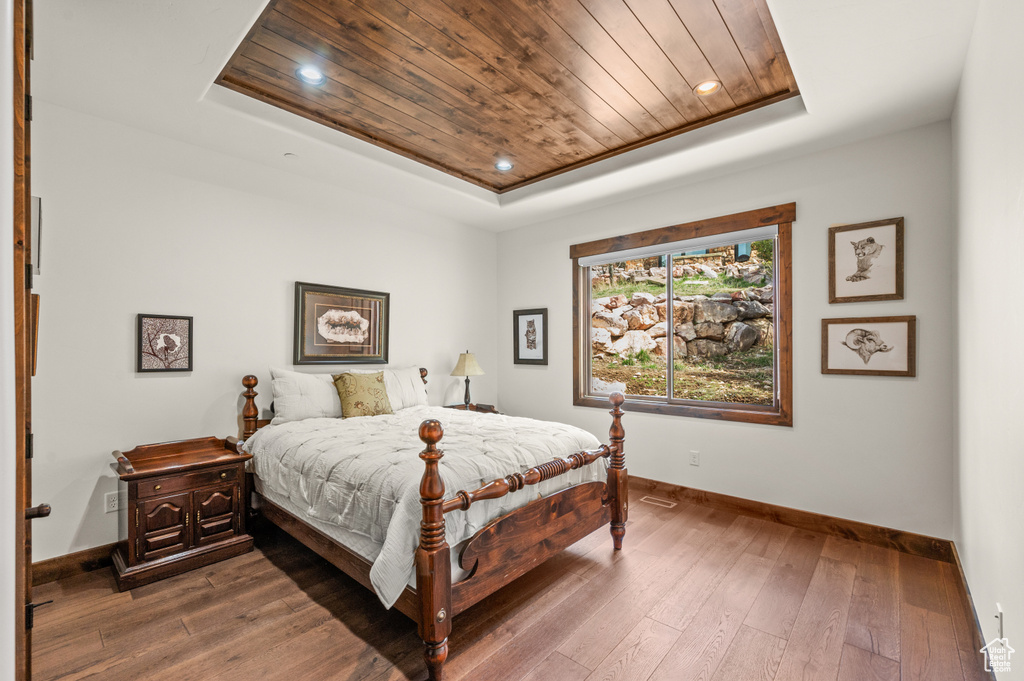 Bedroom with dark wood-type flooring, wood ceiling, and a raised ceiling
