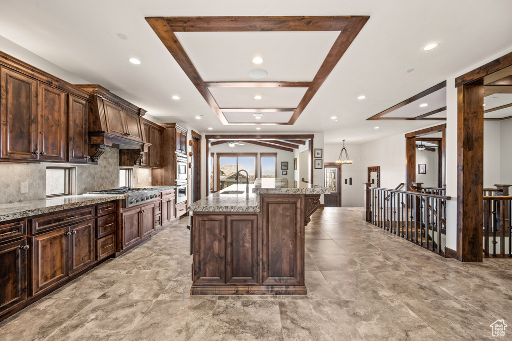 Kitchen with appliances with stainless steel finishes, backsplash, sink, a kitchen island with sink, and light stone countertops