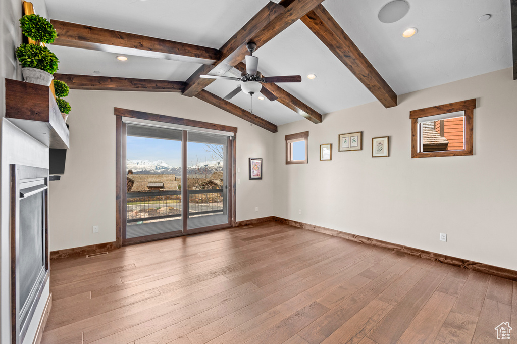 Unfurnished room featuring light hardwood / wood-style flooring, ceiling fan, and lofted ceiling with beams