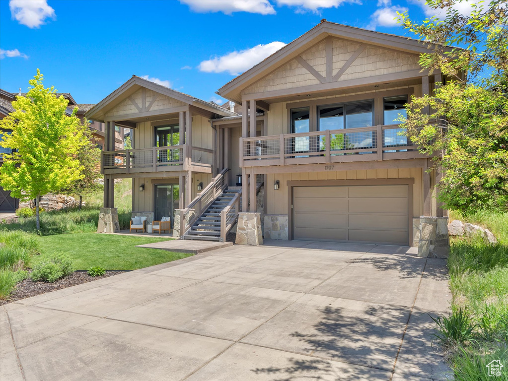 View of front of home with stone siding, an attached garage, stairs, driveway, and a front lawn