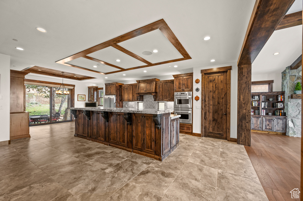 Kitchen featuring a large island with sink, a breakfast bar area, a notable chandelier, stainless steel appliances, and dark stone countertops
