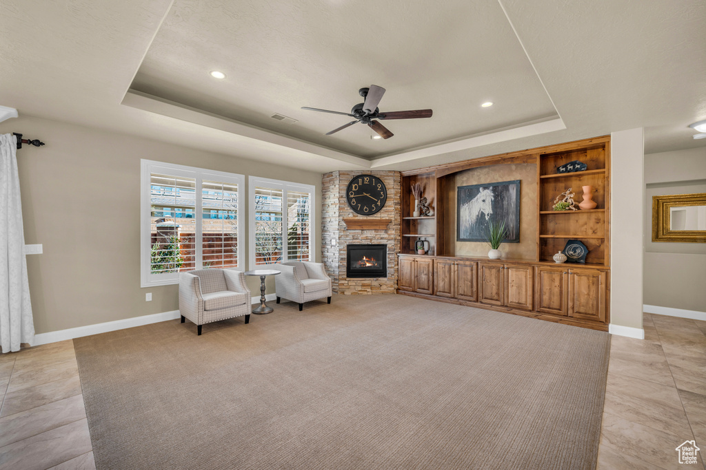 Tiled living room featuring brick wall, ceiling fan, a tray ceiling, and a fireplace
