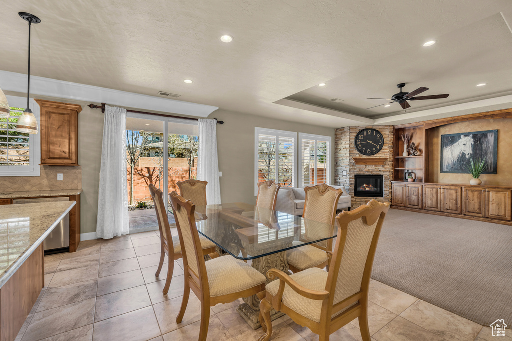 Tiled dining area with built in features, ceiling fan, a fireplace, brick wall, and a tray ceiling