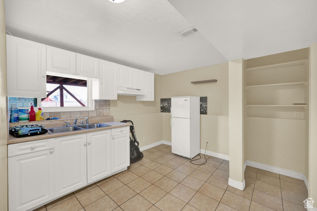 Kitchen with white fridge, light tile flooring, tasteful backsplash, white cabinets, and sink