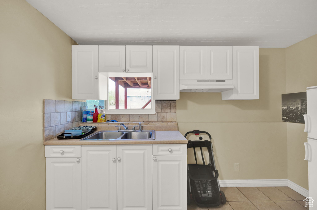 Kitchen with premium range hood, white cabinetry, backsplash, light tile floors, and sink