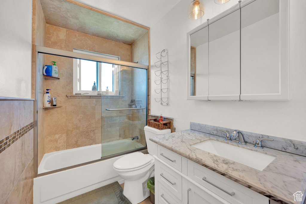 Full bathroom featuring tile flooring, large vanity, toilet, and bath / shower combo with glass door
