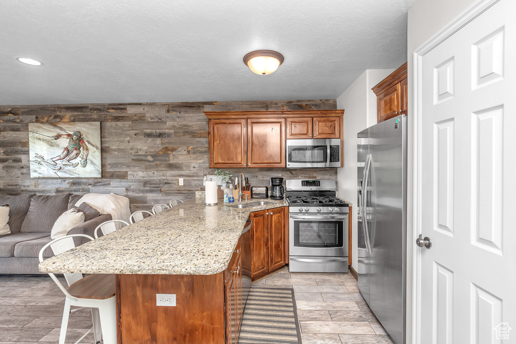Kitchen with a breakfast bar, appliances with stainless steel finishes, light stone counters, wooden walls, and sink