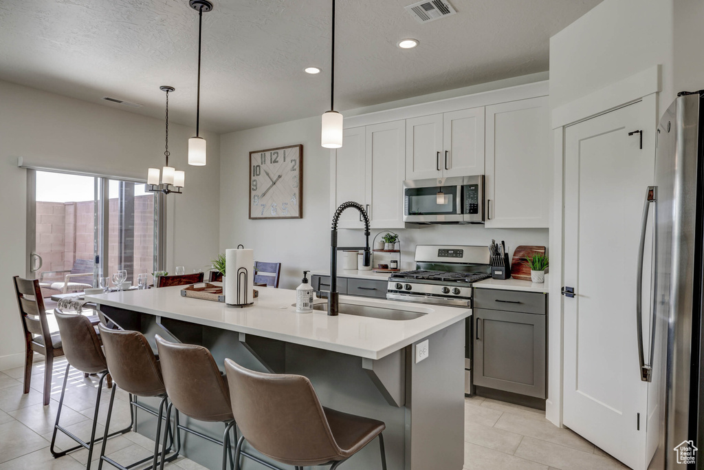 Kitchen featuring pendant lighting, stainless steel appliances, a center island with sink, and a notable chandelier