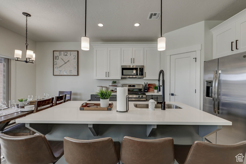 Kitchen featuring pendant lighting, a breakfast bar, stainless steel appliances, a notable chandelier, and white cabinetry