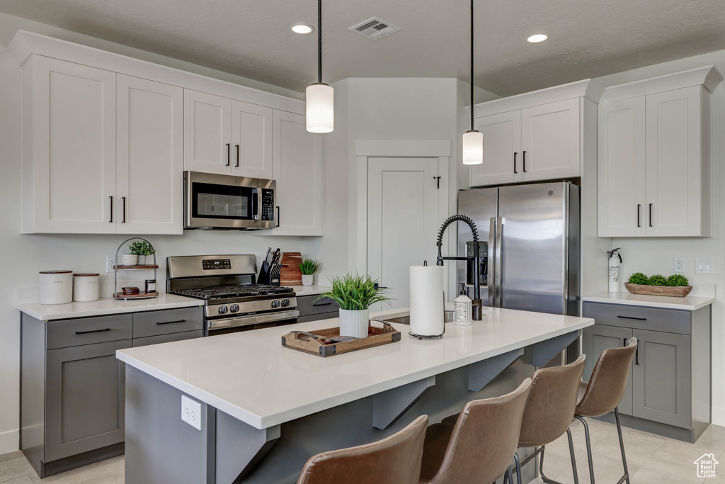 Kitchen featuring decorative light fixtures, a kitchen breakfast bar, an island with sink, light tile floors, and stainless steel appliances