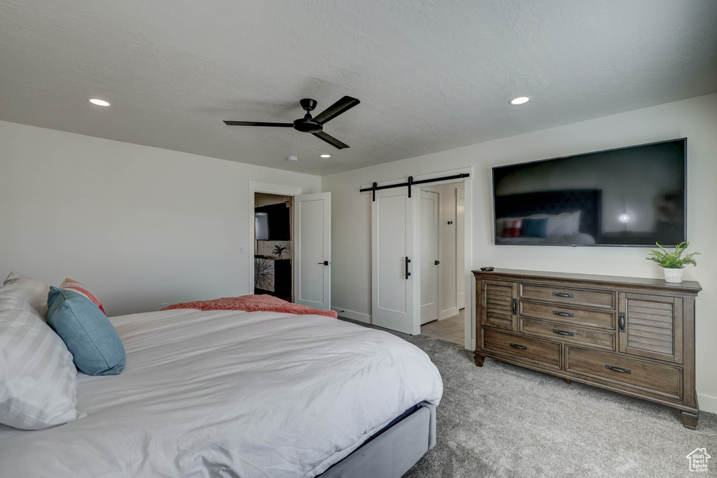 Bedroom with a barn door, ceiling fan, and light colored carpet