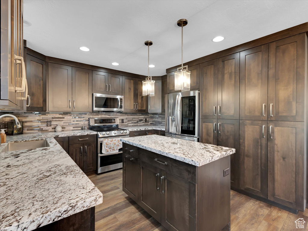 Kitchen with light stone countertops, stainless steel appliances, a center island, and decorative light fixtures
