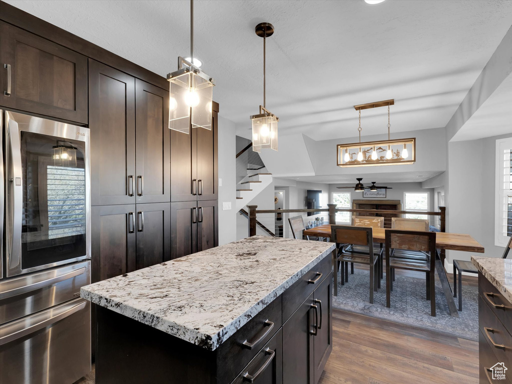 Kitchen featuring pendant lighting, stainless steel refrigerator, a kitchen island, light stone countertops, and dark hardwood / wood-style floors