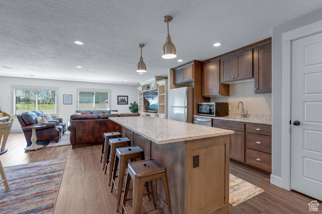 Kitchen featuring appliances with stainless steel finishes, hanging light fixtures, a kitchen island, a kitchen bar, and hardwood / wood-style flooring