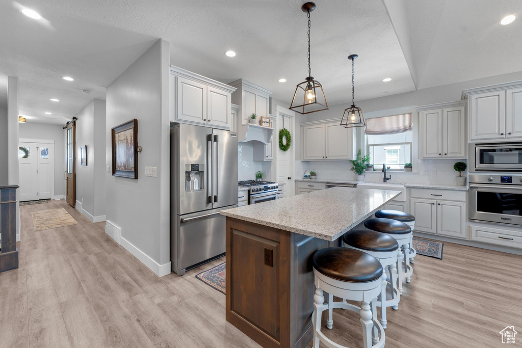 Kitchen with decorative light fixtures, white cabinetry, premium appliances, a center island, and light wood-type flooring