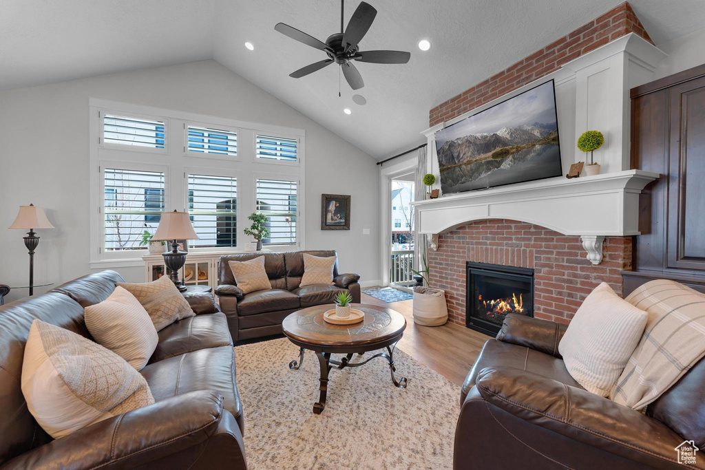 Living room with ceiling fan, light wood-type flooring, a fireplace, and vaulted ceiling