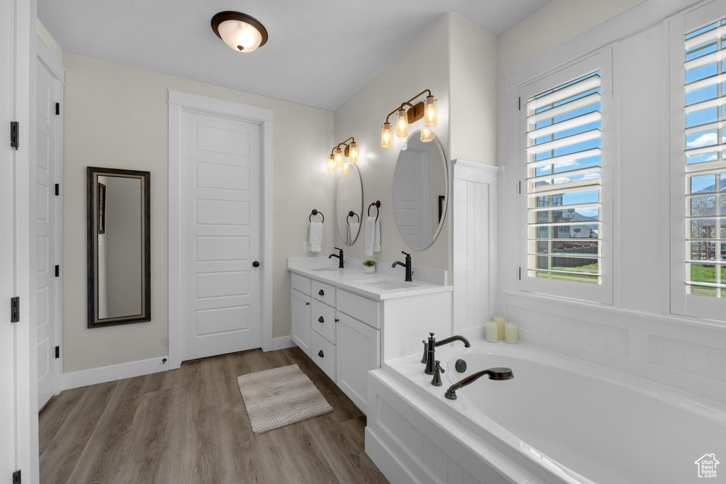 Bathroom featuring tiled bath, double sink, hardwood / wood-style floors, and vanity with extensive cabinet space