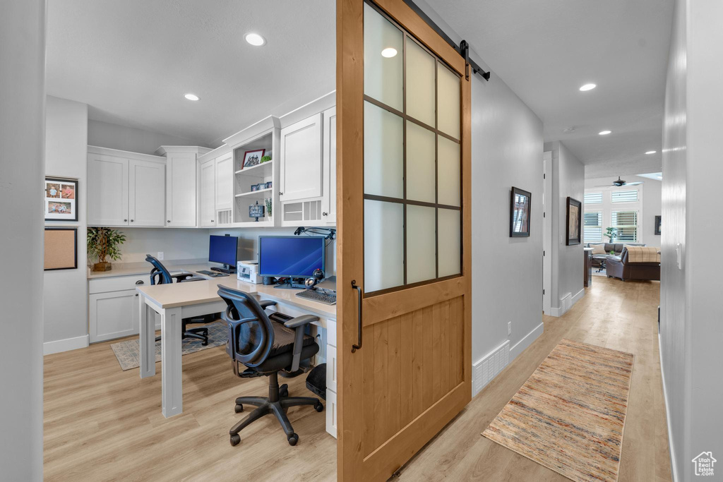 Office space with a barn door, ceiling fan, built in desk, and light hardwood / wood-style floors