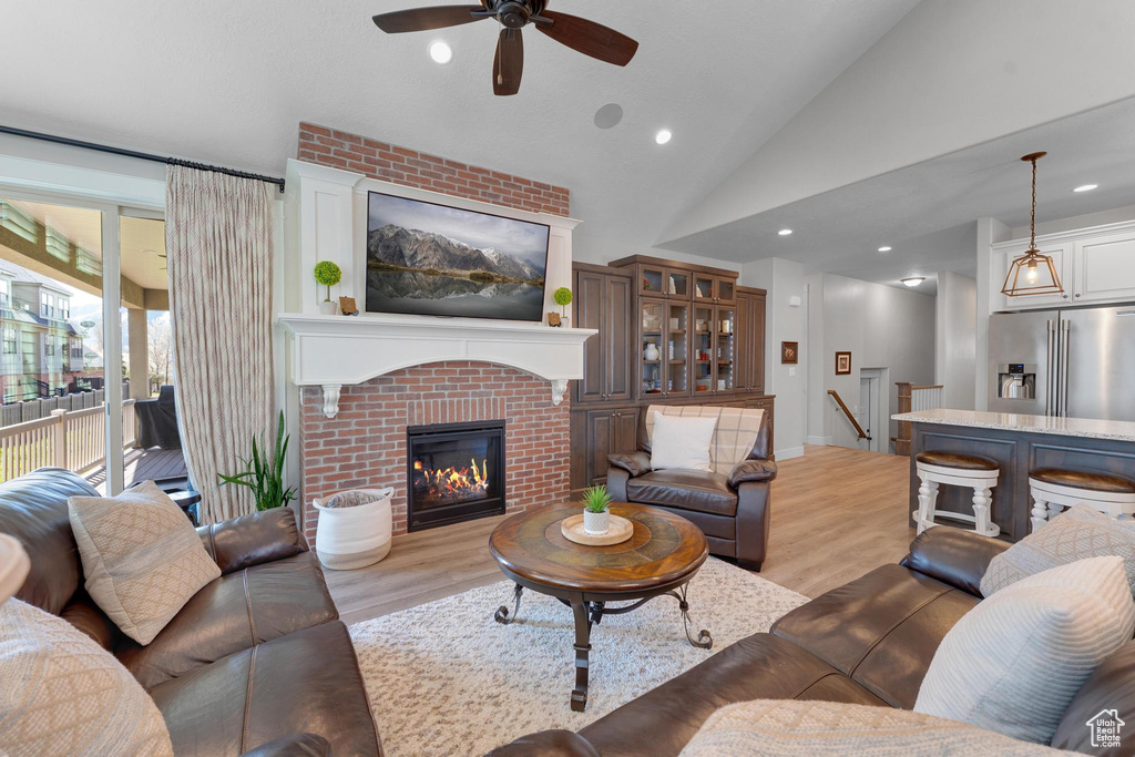 Living room with ceiling fan, lofted ceiling, a brick fireplace, and light wood-type flooring
