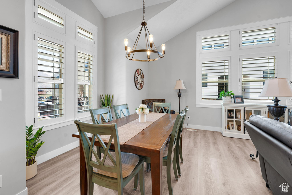 Dining room with a notable chandelier, light hardwood / wood-style floors, vaulted ceiling, and plenty of natural light