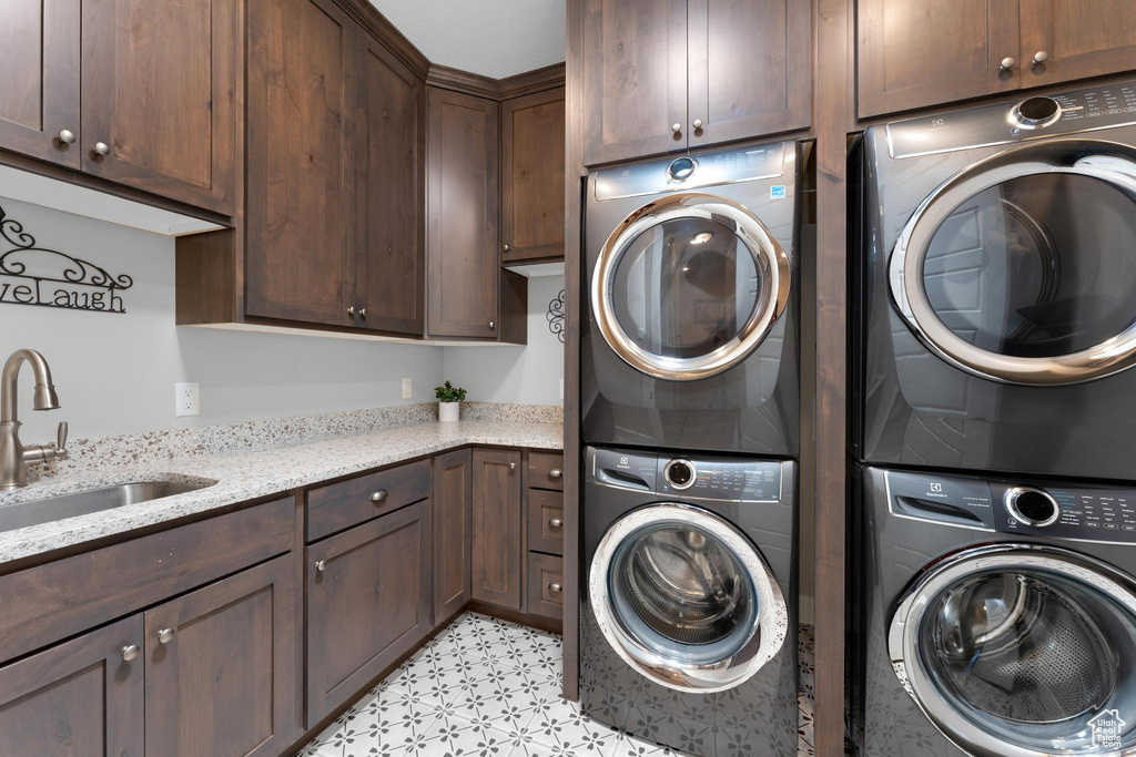 Washroom featuring cabinets, light tile floors, stacked washer / dryer, and sink