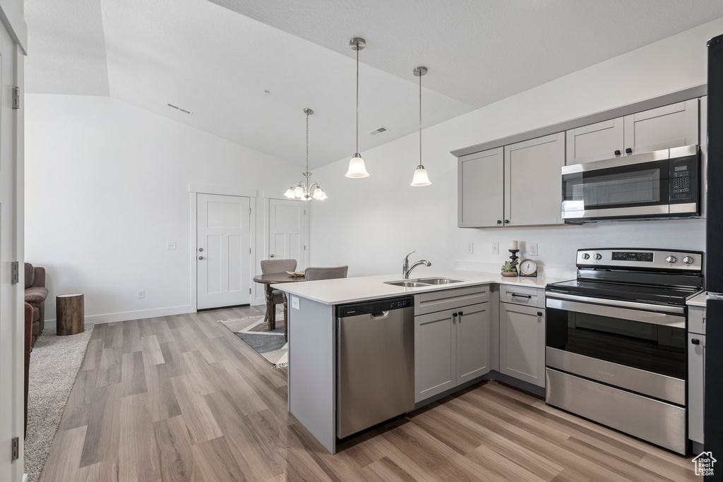 Kitchen with gray cabinetry, stainless steel appliances, light wood-type flooring, and pendant lighting