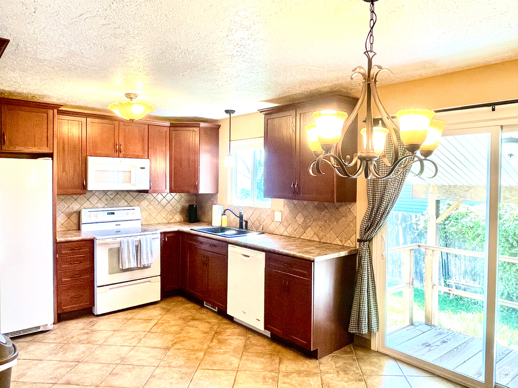 Kitchen with backsplash, sink, light tile flooring, white appliances, and hanging light fixtures