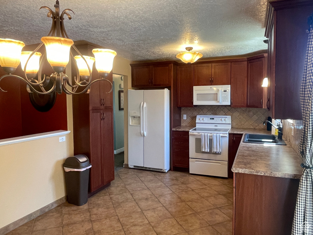 Kitchen with an inviting chandelier, sink, white appliances, tasteful backsplash, and hanging light fixtures