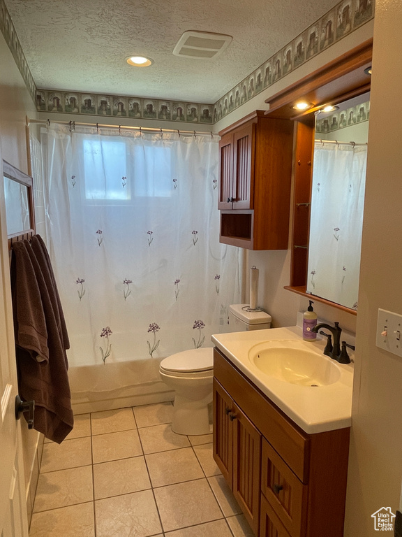 Full bathroom with oversized vanity, shower / bath combo with shower curtain, toilet, a textured ceiling, and tile floors