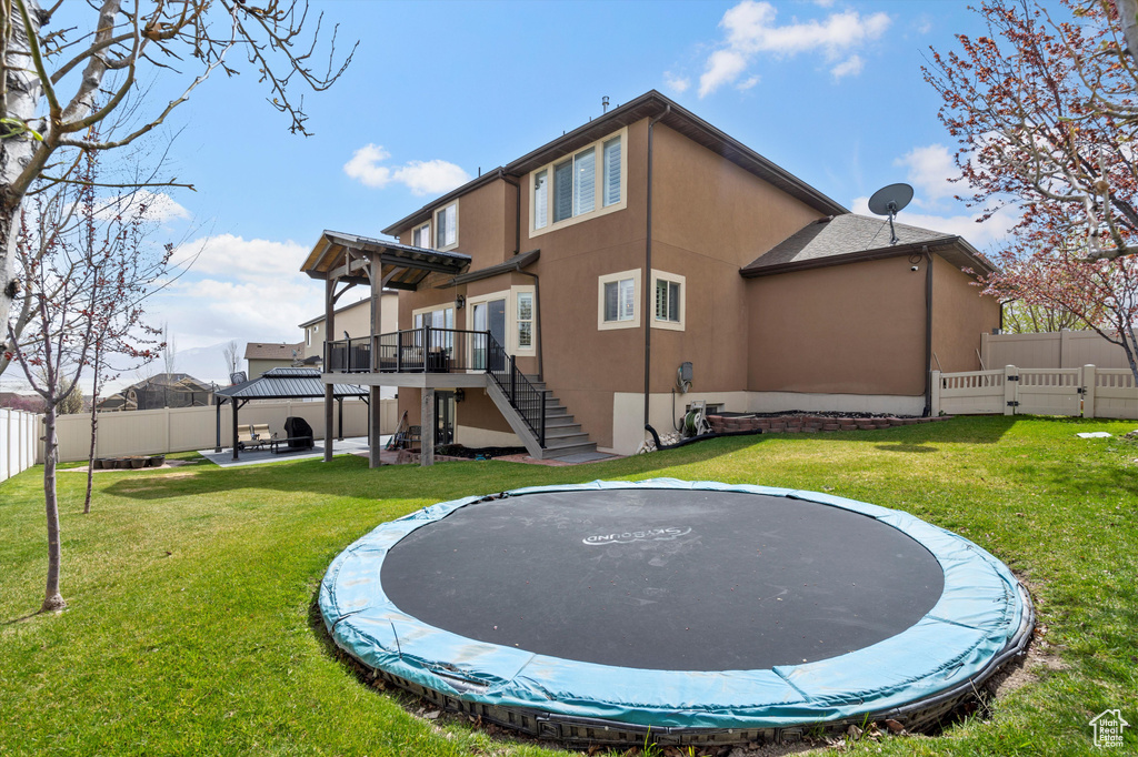Rear view of house with a trampoline, a yard, a deck, and a patio