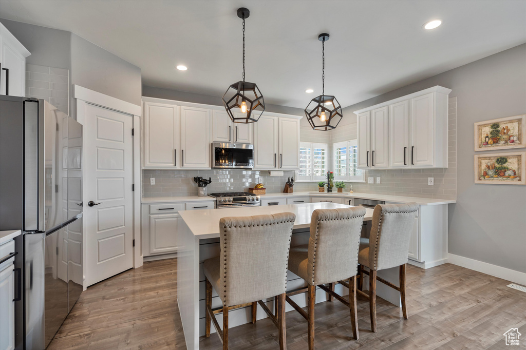 Kitchen with appliances with stainless steel finishes, light wood-type flooring, decorative light fixtures, and white cabinetry