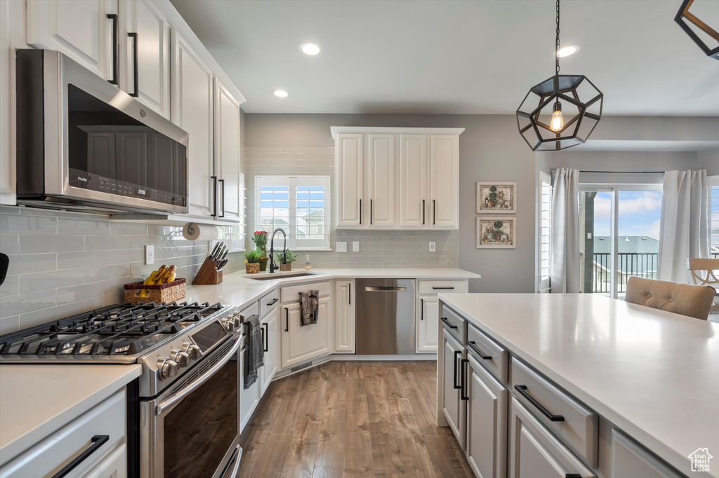 Kitchen with stainless steel appliances, hardwood / wood-style flooring, white cabinetry, tasteful backsplash, and hanging light fixtures