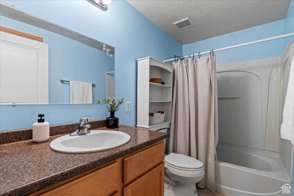 Full bathroom featuring toilet, tile flooring, shower / tub combo with curtain, vanity with extensive cabinet space, and a textured ceiling