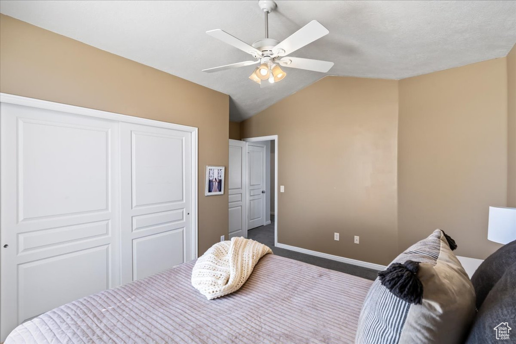 Carpeted bedroom with ceiling fan, a closet, and vaulted ceiling
