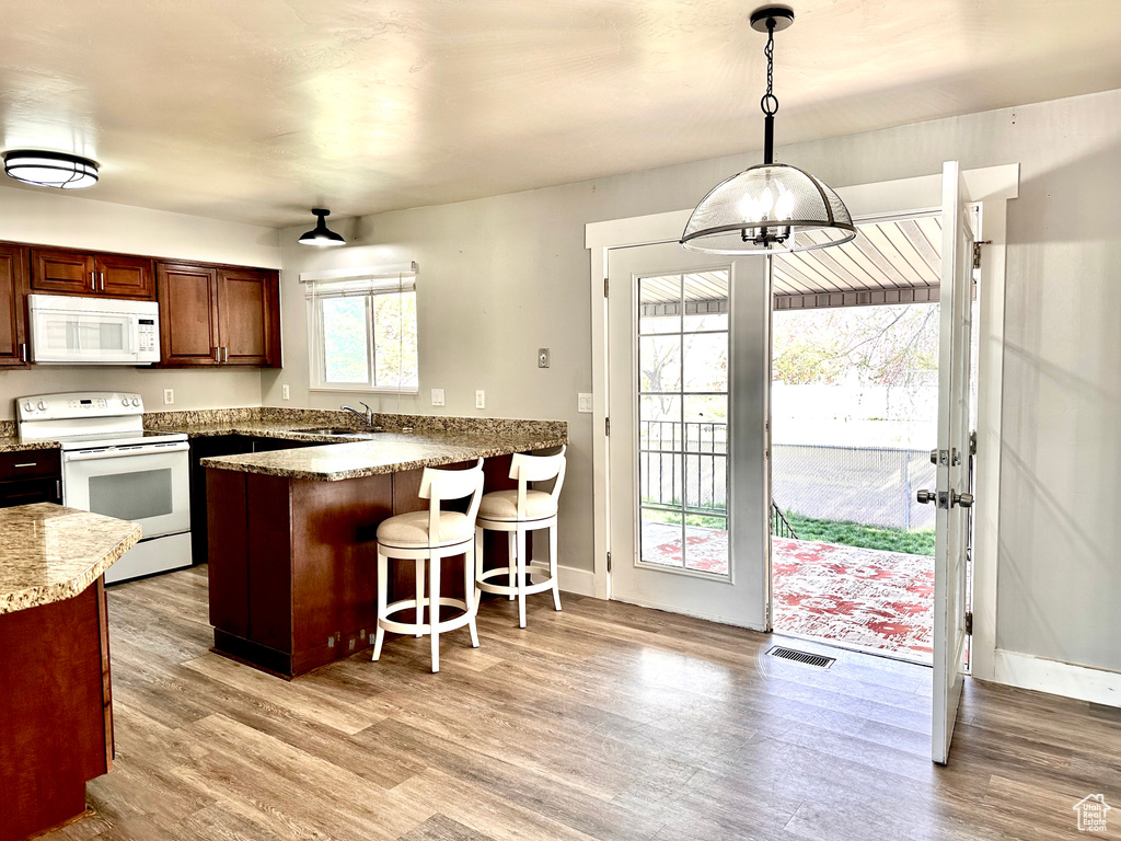Kitchen featuring light hardwood / wood-style flooring, white appliances, a kitchen breakfast bar, sink, and pendant lighting