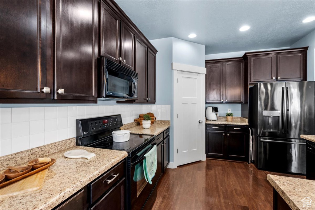 Kitchen featuring black appliances, dark brown cabinetry, dark hardwood / wood-style floors, light stone counters, and tasteful backsplash