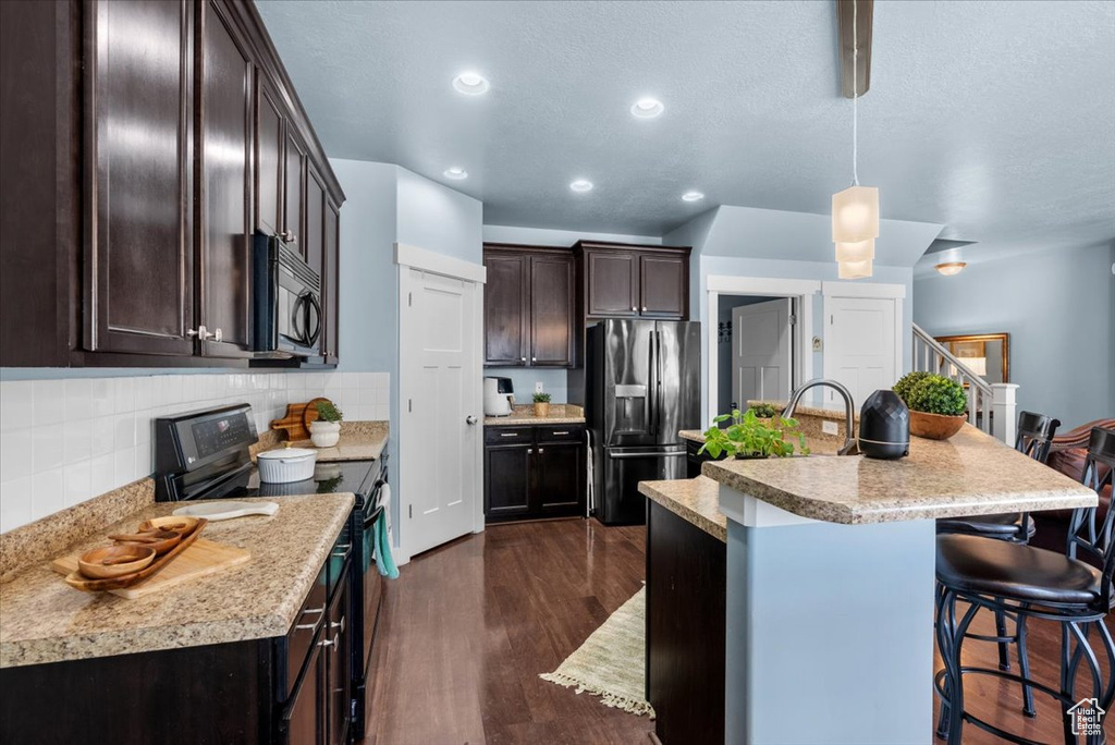 Kitchen featuring appliances with stainless steel finishes, hanging light fixtures, backsplash, a kitchen bar, and dark hardwood / wood-style flooring