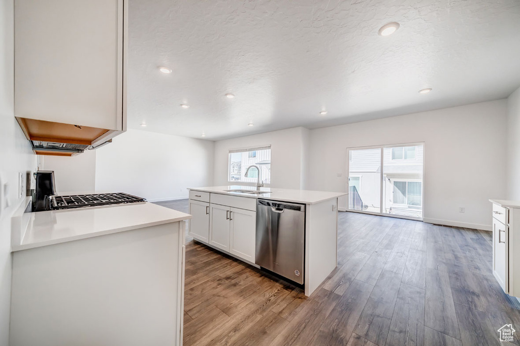 Kitchen featuring light hardwood / wood-style floors, white cabinets, stainless steel dishwasher, plenty of natural light, and a kitchen island with sink