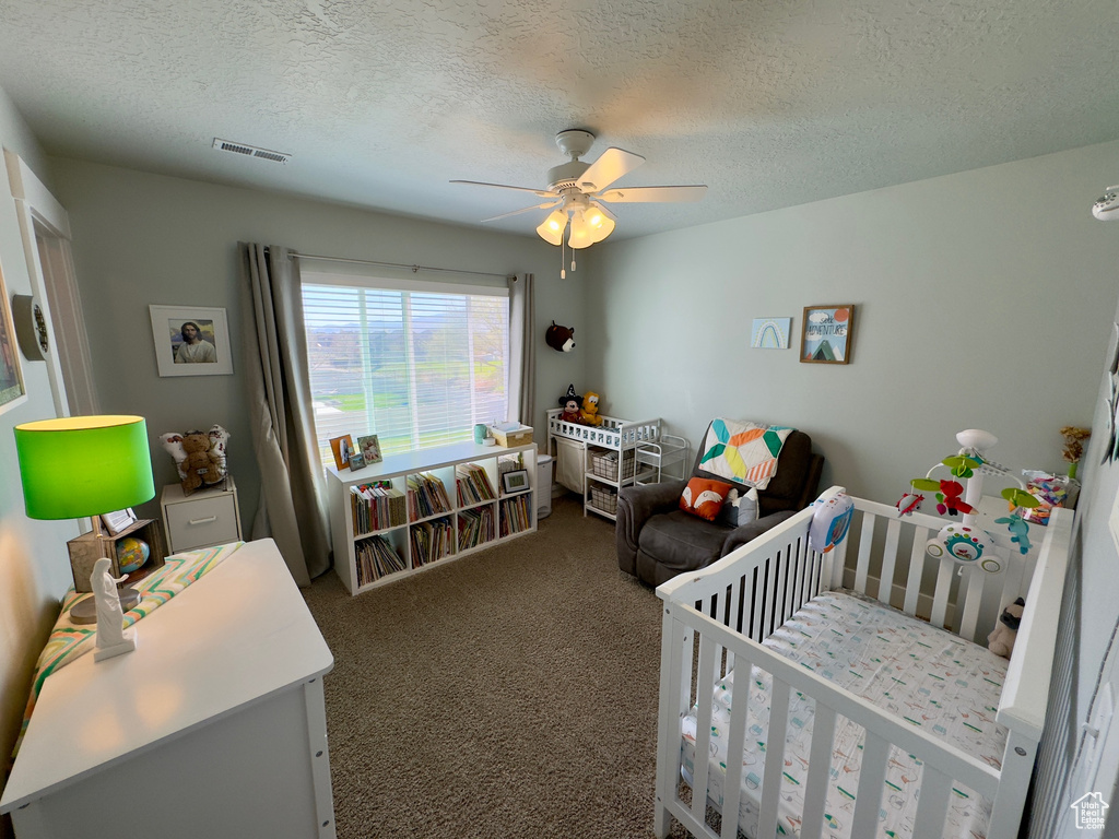 Carpeted bedroom with ceiling fan, a crib, and a textured ceiling