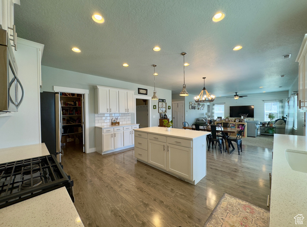 Kitchen with white cabinets, backsplash, a center island, pendant lighting, and hardwood / wood-style floors