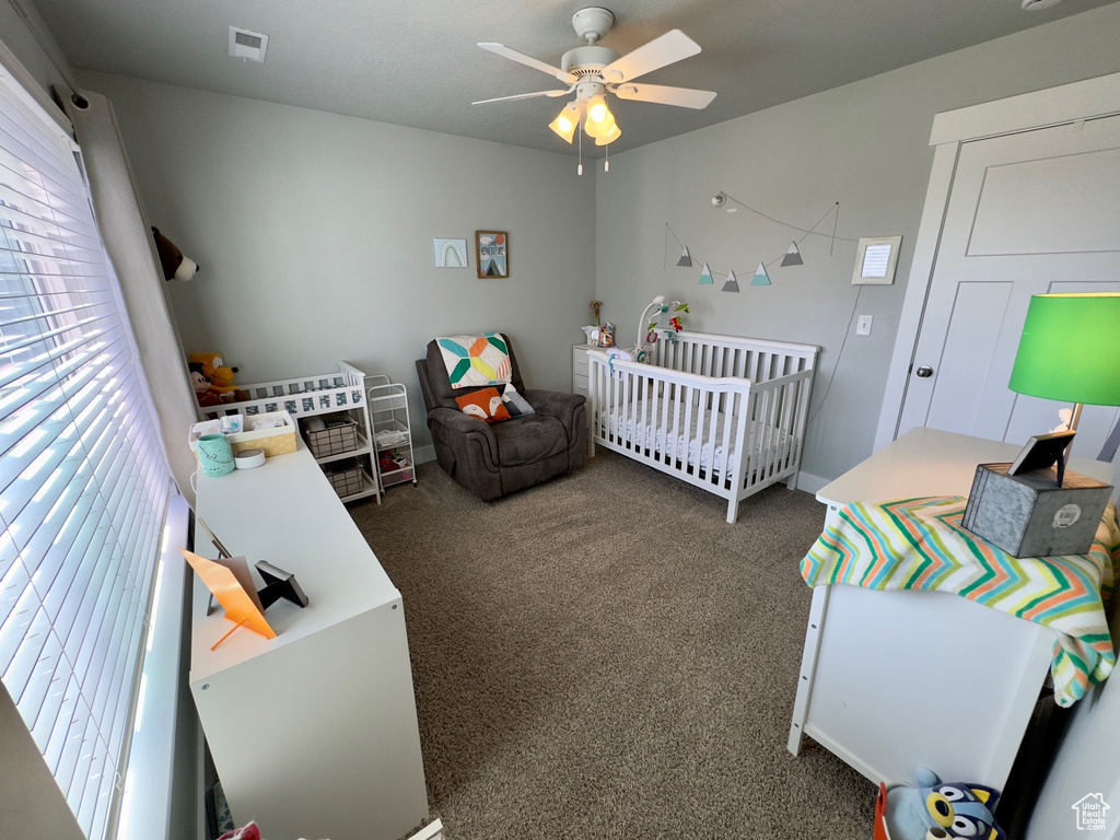 Carpeted bedroom featuring ceiling fan and a crib
