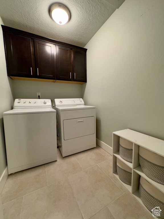 Clothes washing area featuring light tile flooring, cabinets, separate washer and dryer, and a textured ceiling