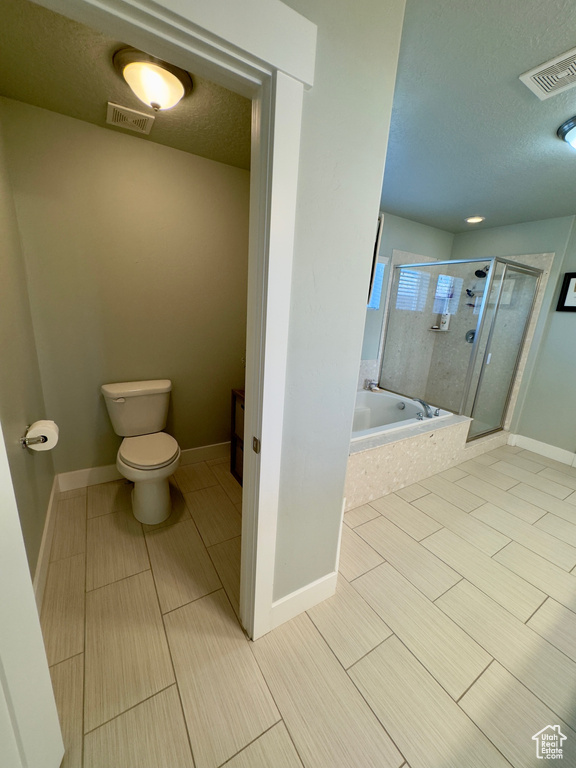 Bathroom featuring separate shower and tub, tile floors, toilet, and a textured ceiling