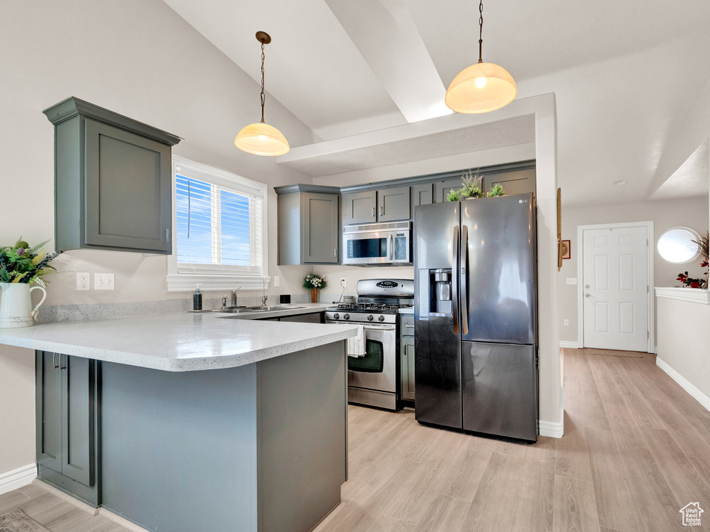Kitchen with appliances with stainless steel finishes, light hardwood / wood-style floors, decorative light fixtures, and kitchen peninsula