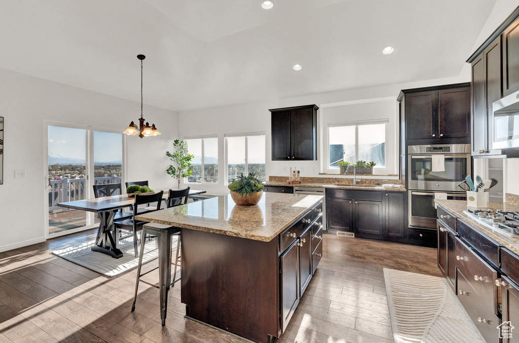 Kitchen featuring decorative light fixtures, light stone counters, light hardwood / wood-style floors, stainless steel appliances, and a center island