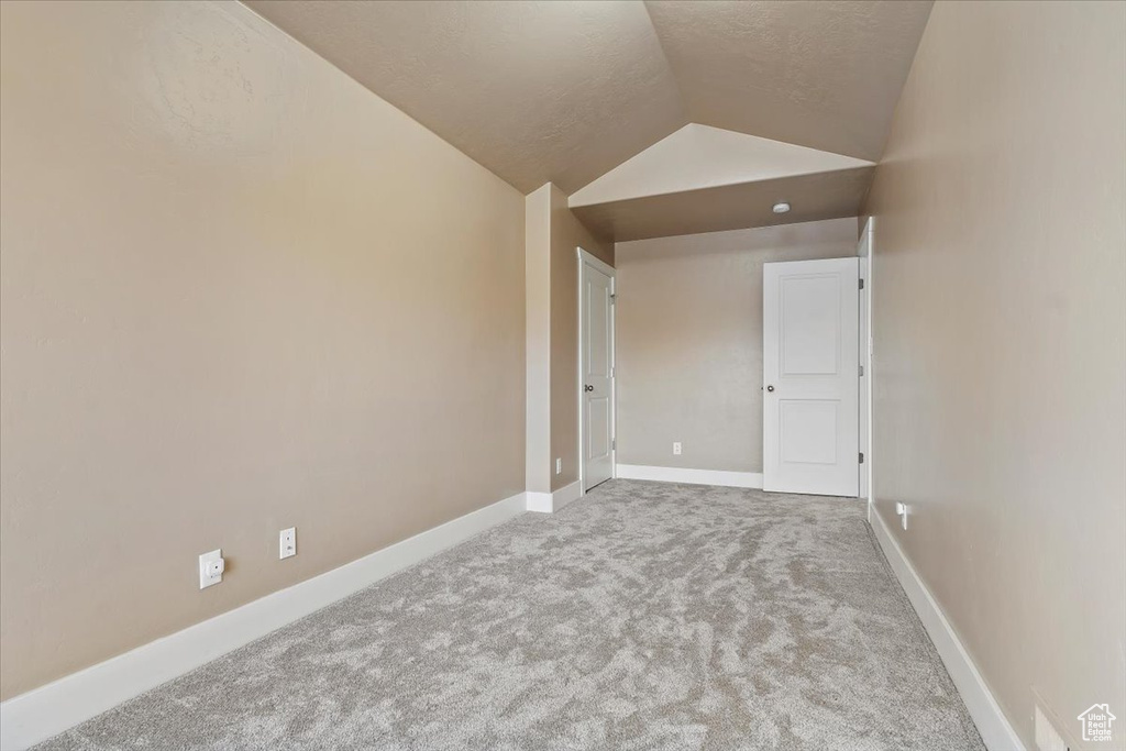 Carpeted empty room featuring vaulted ceiling and a textured ceiling