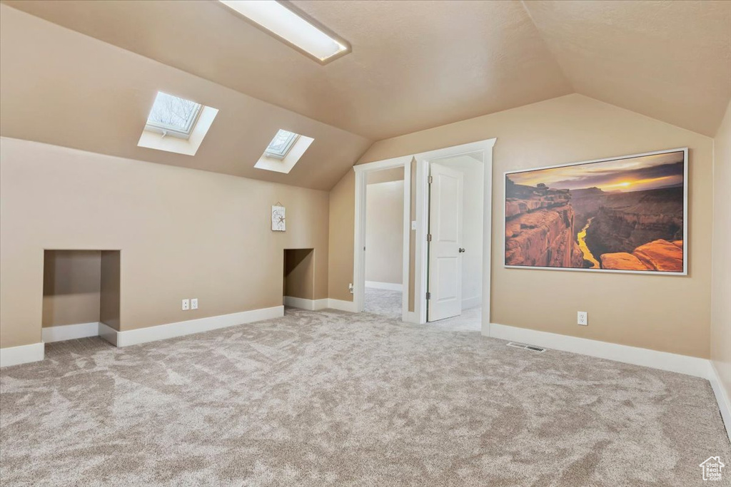 Additional living space with light carpet and vaulted ceiling with skylight