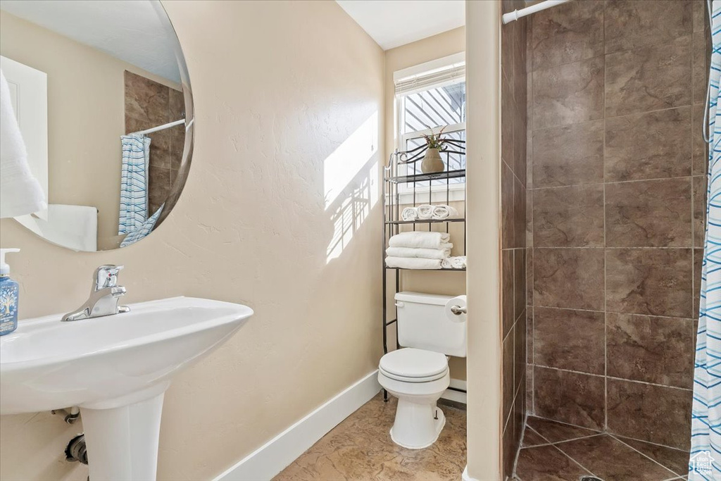 Bathroom featuring a shower with curtain, toilet, tile floors, and sink