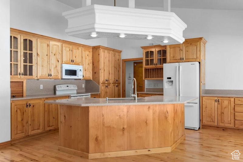 Kitchen featuring light hardwood / wood-style flooring, a kitchen island with sink, white appliances, high vaulted ceiling, and tasteful backsplash